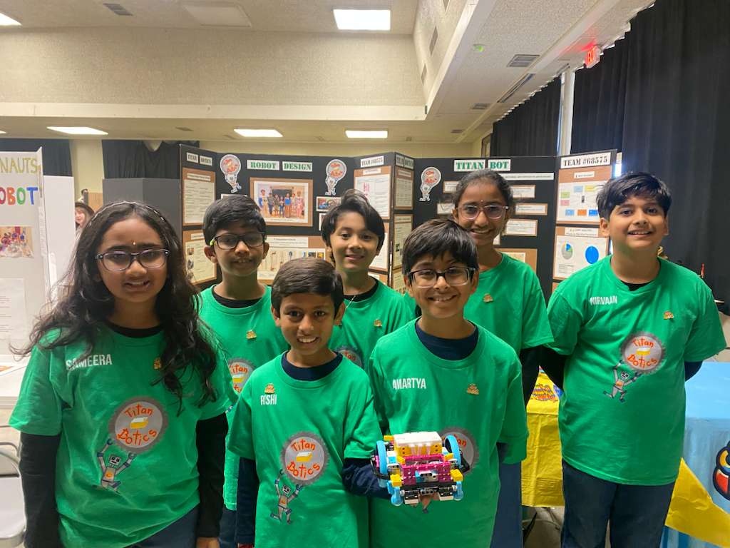 The seven UNEARTHED teammates in green Titanbotics shirts, with their LEGO robot